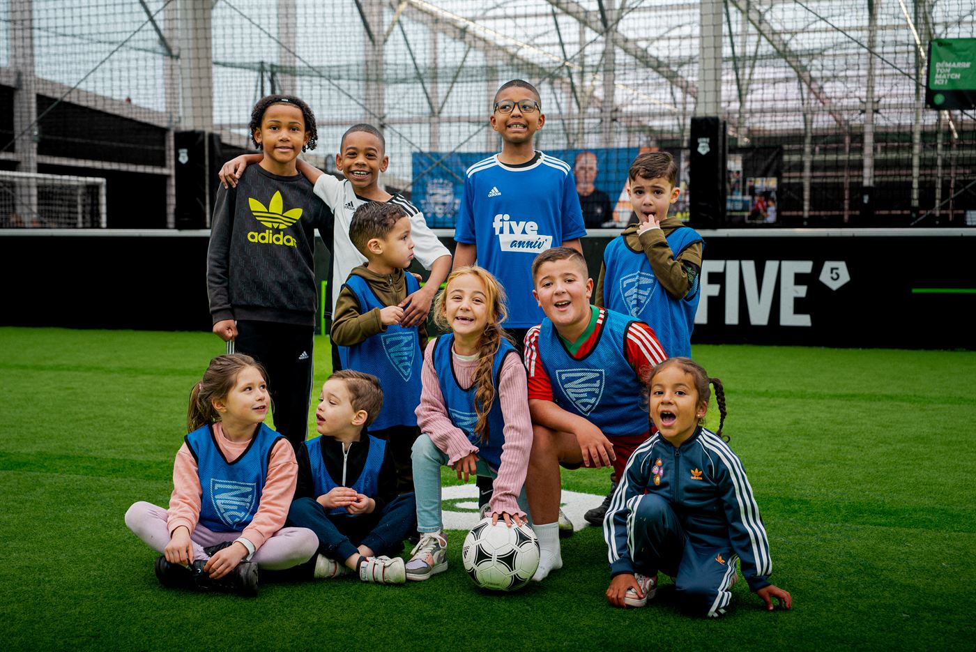 Groupe d’enfants en chasuble autour d’un ballon, sur un terrain de foot